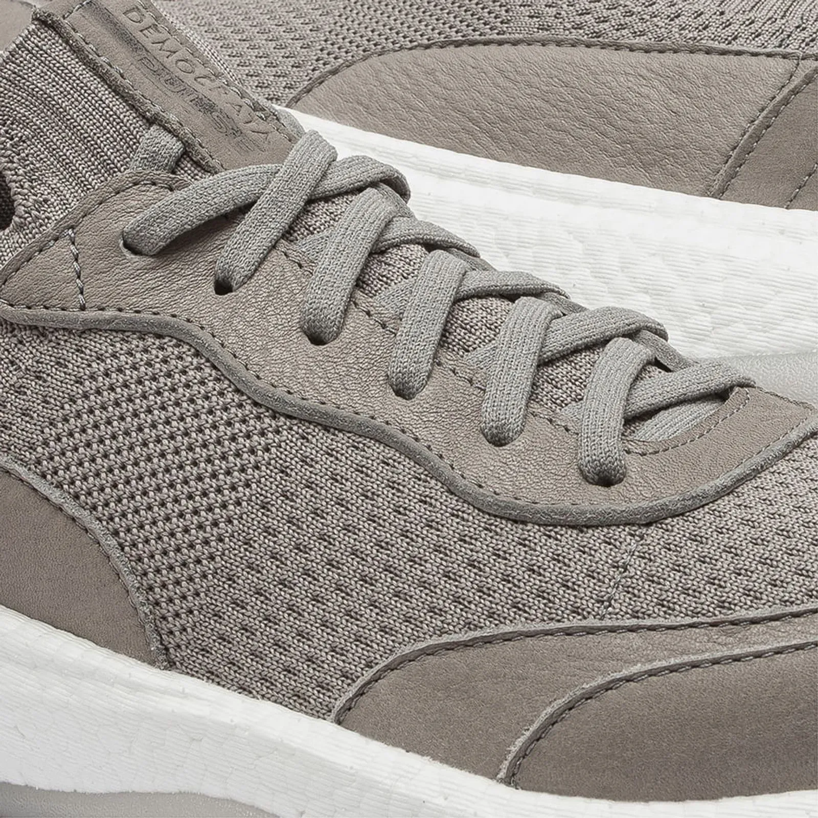Detalhe do tênis Democrata Knit Draft Pulse Cinza Masculino mostrando textura de malha e fechamento por atacadores elásticos.